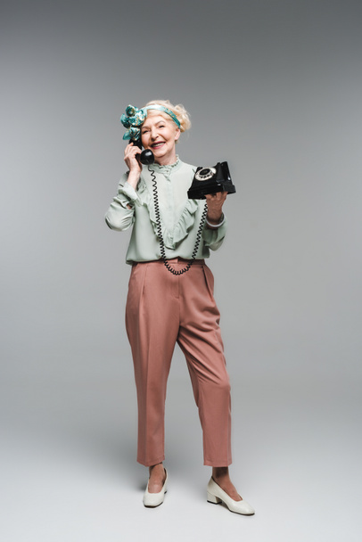 mulher sênior feliz falando por telefone rotativo em cinza
 - Foto, Imagem