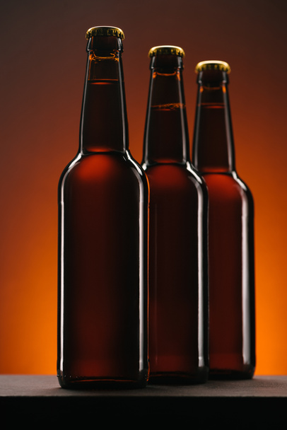 close up view of arranged bottles of beer on orange backdrop - Zdjęcie, obraz