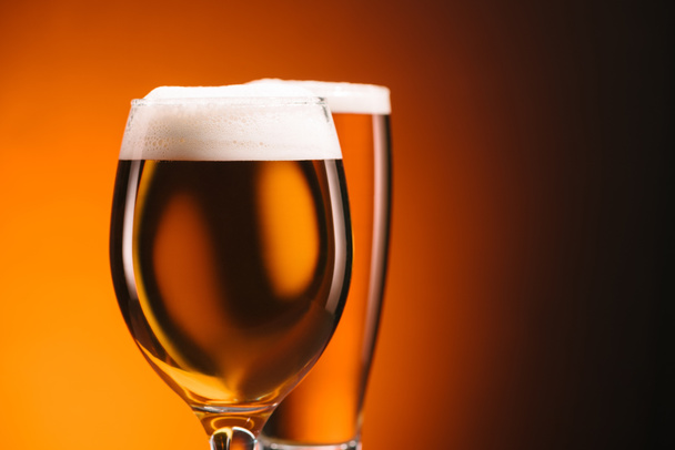 close up view of arrangement of glasses of beer on orange backdrop - 写真・画像