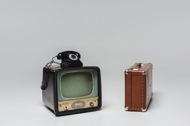 παλιάς χρονολογίας τηλεόραση με περιστροφικό τηλέφωνο και βαλίτσα σε γκρι - Φωτογραφία, εικόνα