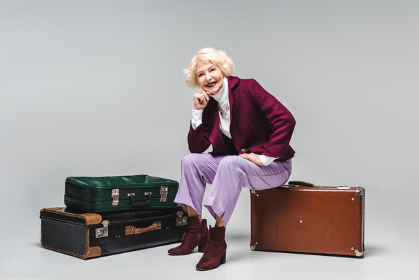 beautiful senior woman sitting on vintage suitcase on grey - Фото, зображення