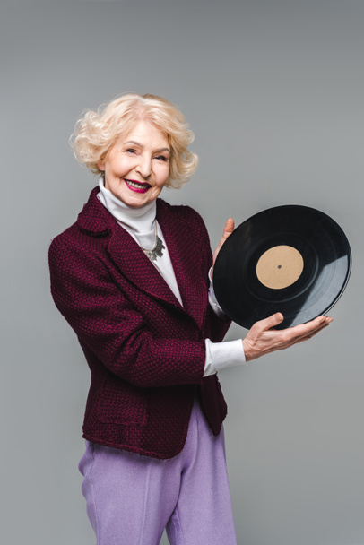 beautiful senior woman holding vinyl disc isolated on grey - Foto, Imagen