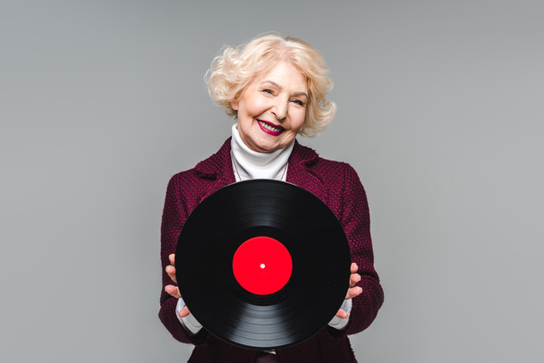 mujer mayor con estilo sosteniendo disco de vinilo aislado sobre fondo gris
  - Foto, imagen