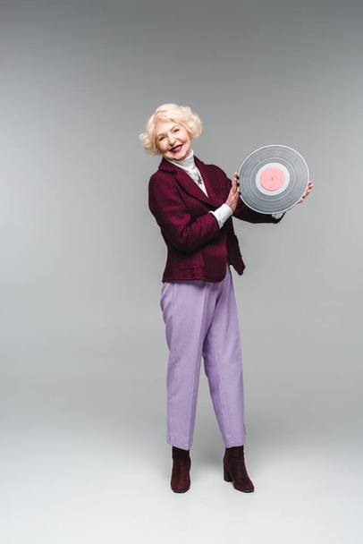happy stylish senior woman holding vinyl disc on gray background  - Zdjęcie, obraz