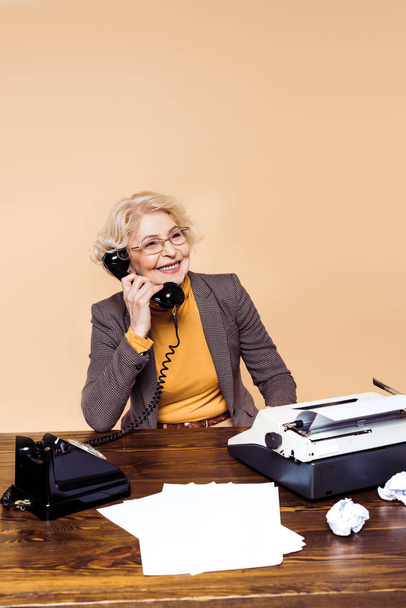 s úsměvem elegantní starší žena v brýlích mluvit na telefonu u stolu  - Fotografie, Obrázek