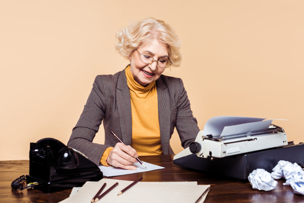 κομψή γυναίκα ανώτερος γραψίματος σε χαρτί στο τραπέζι με γραφομηχανή και περιστροφικό τηλέφωνο - Φωτογραφία, εικόνα