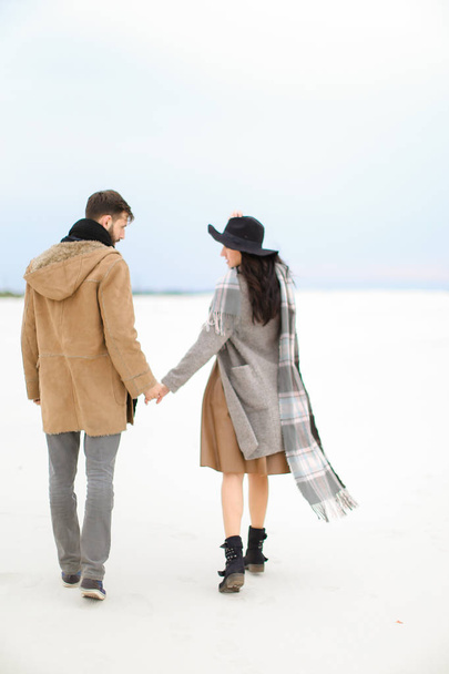 Szczęśliwa kobieta i mężczyzna chodzenia po śniegu i trzymając się za ręce, na sobie płaszcz, szary szalik i czapka. - Zdjęcie, obraz