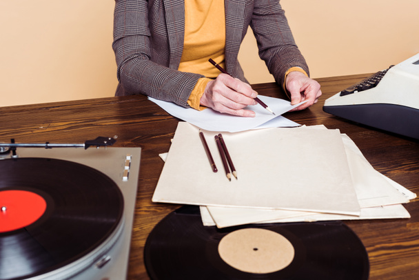 cropped image of woman writing in paper at table with vinyl disc, record player and typewriter  - Фото, изображение