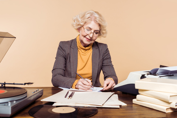 femme âgée en lunettes écrivant en papier à table avec disque vinyle, tourne-disque et machine à écrire
  - Photo, image