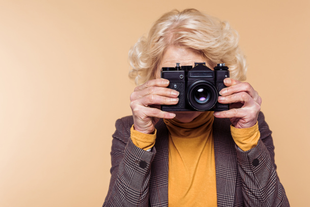 Senior vrouw schieten op filmcamera geïsoleerd op beige achtergrond  - Foto, afbeelding