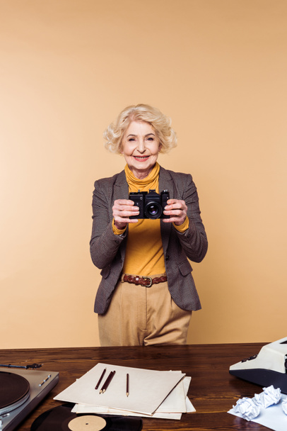 χαμογελώντας κομψή γυναίκα ανώτερος με απομονωμένα σε μπεζ φόντο φωτογραφική μηχανή ταινία - Φωτογραφία, εικόνα