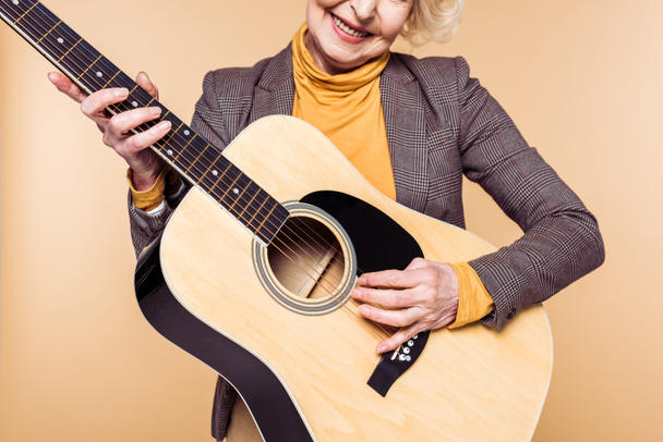 обрезанный образ стильной женщины, играющей на акустической гитаре на бежевом фоне
  - Фото, изображение