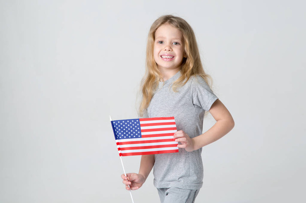 Little girl with the flag of United States of America on a gray background. The blond girl is 6 years old in a light gray shirt - Φωτογραφία, εικόνα