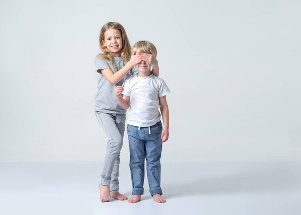 Children, brother and sister standing on a light background. Little girl closed her eyes to the boy. Surprise. - Fotografie, Obrázek