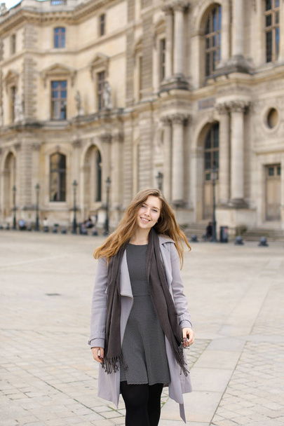 Fiatal nő szürke kabátot áll közel a párizsi Louvre-ban. - Fotó, kép
