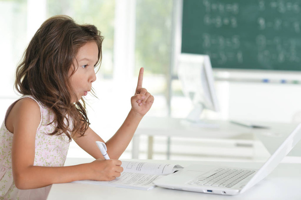 Милая маленькая девочка делает домашнее задание с ноутбуком дома
 - Фото, изображение