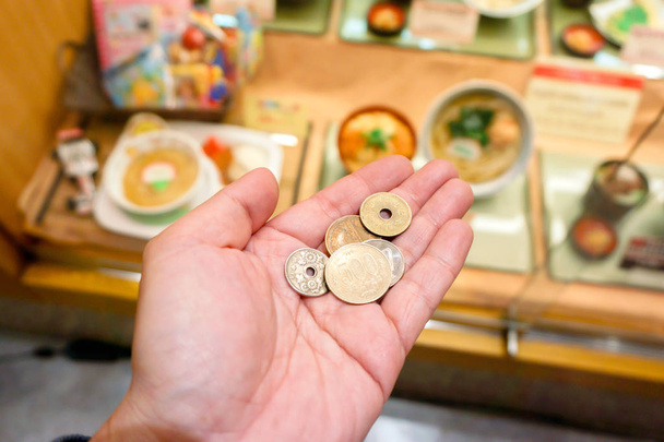 Image from eyes looking Japan Yen coins on hand front of blurry Japanese restaurant display, It shows that the cost of living in Japan is so high and the price of food in restaurants is high too. - Photo, Image