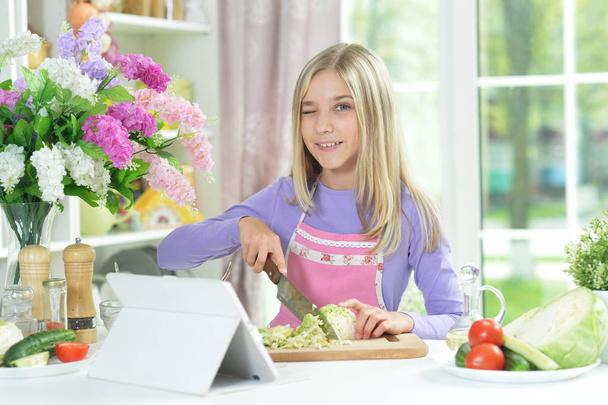 Cute girl preparing fresh salad on kitchen table with tablet at home - Fotografie, Obrázek