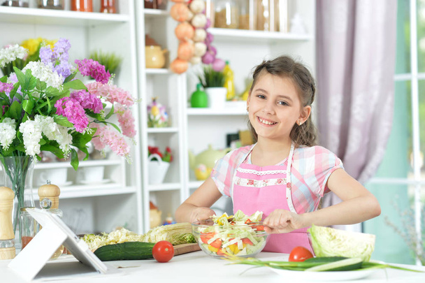 Cute little girl making dinner on kitchen table with  tablet at home - Foto, immagini