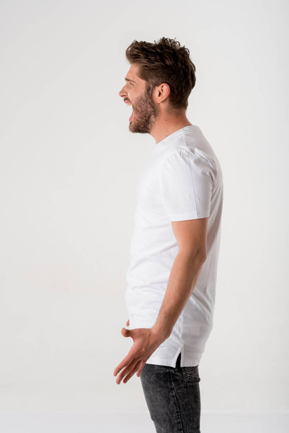 portrait of young bearded man screaming in white shirt on grey background  - Zdjęcie, obraz