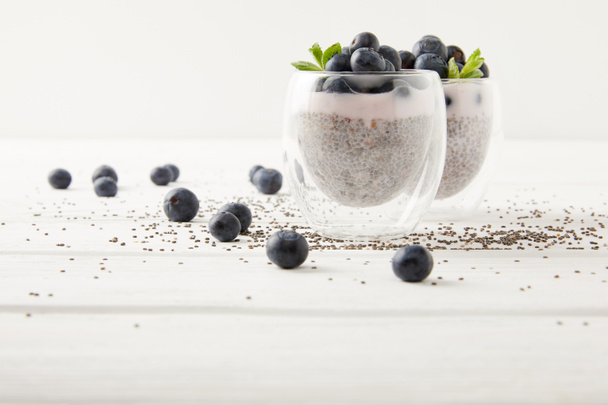 close up view of chia puddings with fresh blueberries and mint on white wooden tabletop - Foto, afbeelding