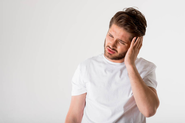 portrait of young bearded man in white shirt with pain in head on grey background - Foto, Imagen