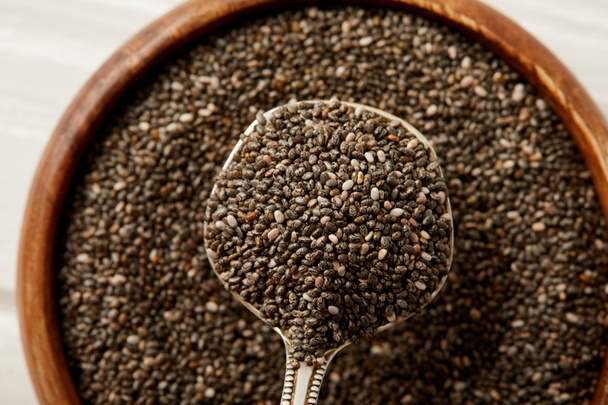 close up view of chia seeds in spoon and wooden bowl - Fotografie, Obrázek