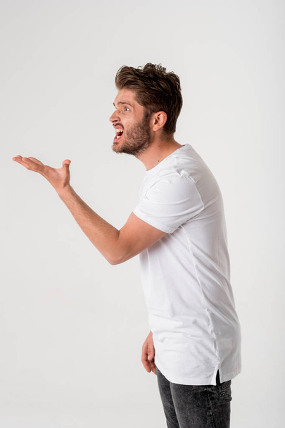 portrait of young bearded disgusted man in white shirt gesture on grey background  - 写真・画像