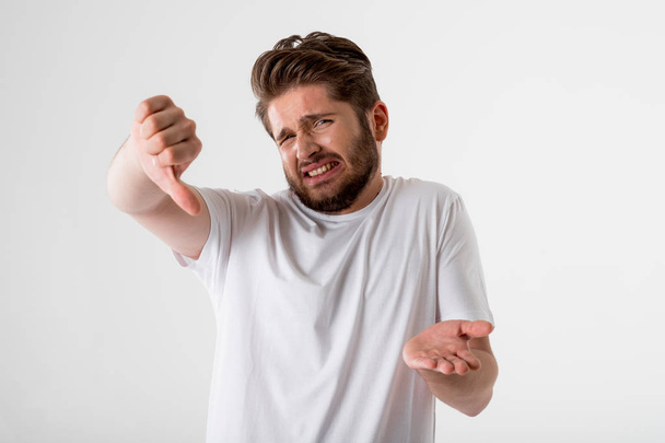 portrait of young bearded man gesture thumbs down in white shirt on grey background  - Fotoğraf, Görsel