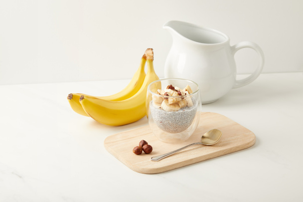 close up view of tasty chia seed pudding with bananas and hazelnuts on white tabletop - 写真・画像