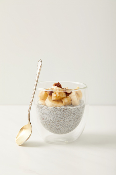 Zobacz smaczne chia seed pudding z kawałkami banana i orzechy laskowe na białym stole z bliska - Zdjęcie, obraz