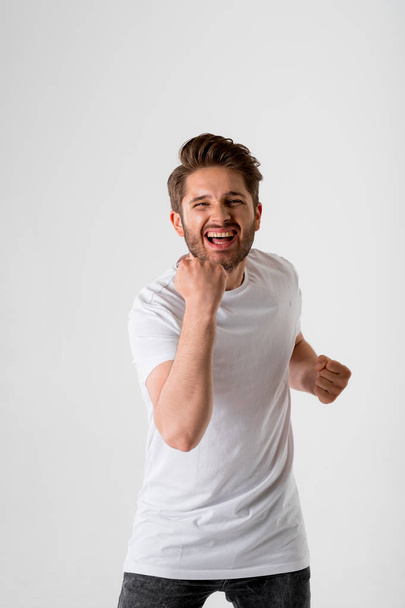 portrait of young bearded unbelievably excited and slightly shocked man in white shirt on grey background - Fotó, kép