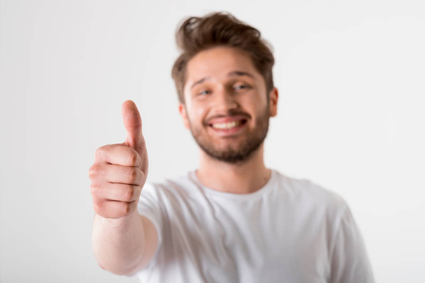 portrait of young bearded man gesture thumbs up in white shirt on grey background  - 写真・画像