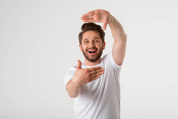 portrait of happy young bearded man gesture frame in white shirt on grey background  - Foto, imagen