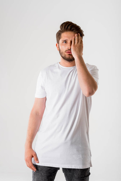 portrait of young frightened bearded man in white shirt holding head on grey background  - Φωτογραφία, εικόνα