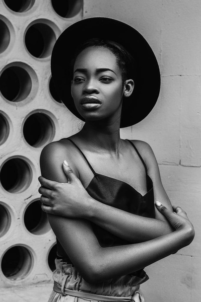 Retrato de modelo feminino africano em chapéu de moda posando ao ar livre em fundo cinza
. - Foto, Imagem