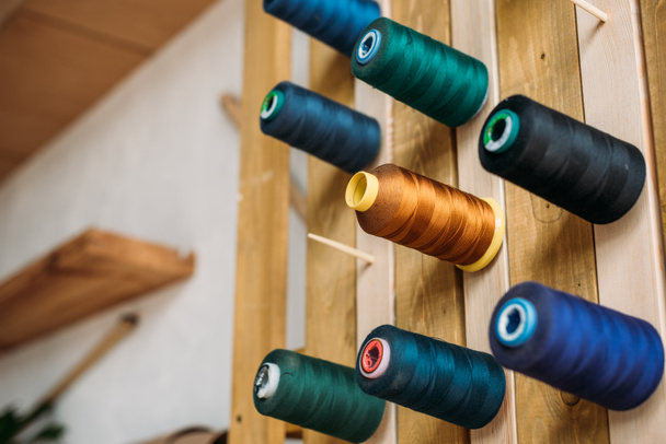 Farbige Fadenspulen hängen an Holzwand in Nähwerkstatt - Foto, Bild
