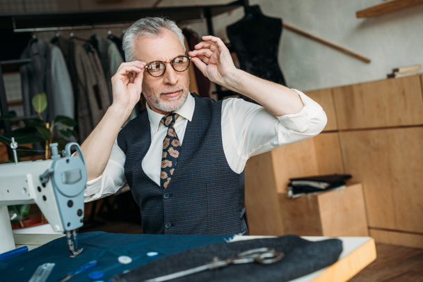 Senior kleermaker dragen van een bril voor het naaien op naaien workshop - Foto, afbeelding