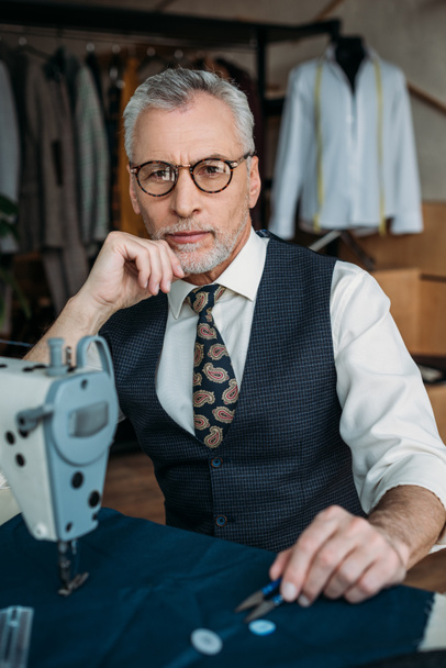 handsome senior tailor looking at camera at sewing workshop - Photo, Image