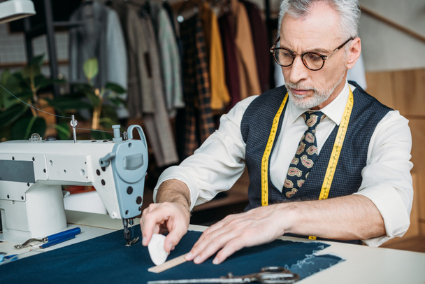 tailleur senior faisant modèle sur tissu avec morceau de craie à l'atelier de couture
 - Photo, image
