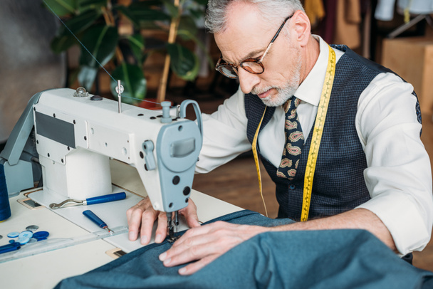 красивый портной в очках швейная ткань с швейной машинкой в швейной мастерской
 - Фото, изображение