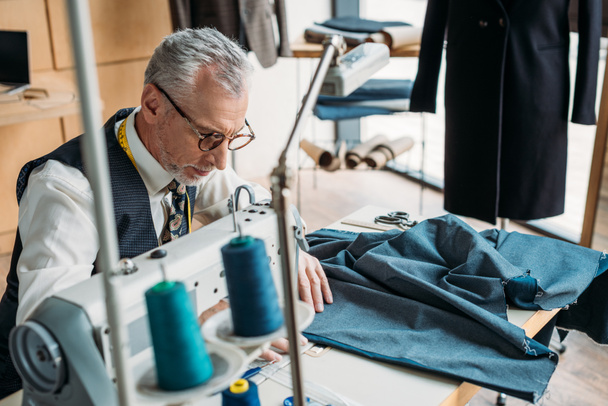 guapo sastre costura paño azul con máquina de coser en taller de costura
 - Foto, Imagen