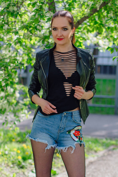Charming woman dressed in a leather jacket near bird-cherry tree - Photo, image
