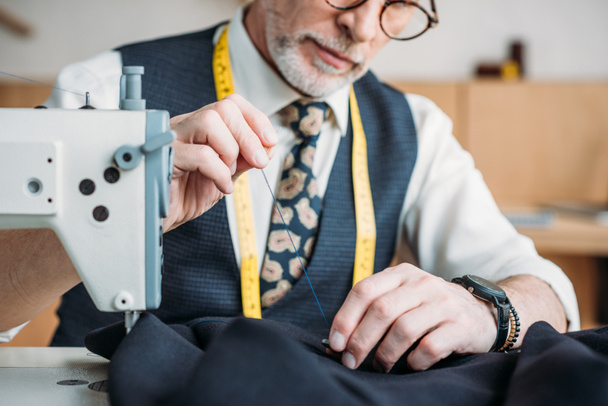immagine ritagliata di sarto senior pulsante di cucito per giacca al laboratorio di cucito
 - Foto, immagini
