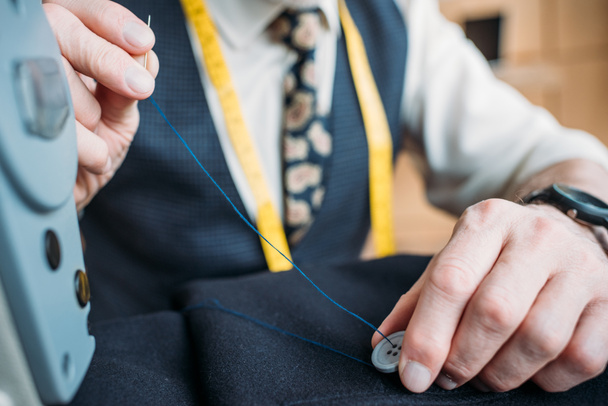cropped image of tailor sewing button to dark blue jacket at sewing workshop - Фото, зображення