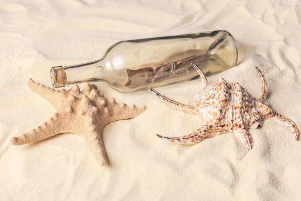 Botella con letra y concha con estrella de mar en la playa de arena
 - Foto, imagen