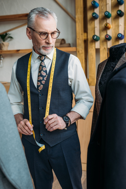 sastre guapo mirando chaquetas en maniquíes en taller de costura
 - Foto, Imagen