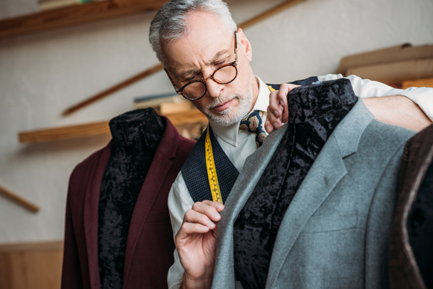 tailleur mature concentré avec ruban à mesurer examinant la veste sur mannequin à l'atelier de couture
 - Photo, image