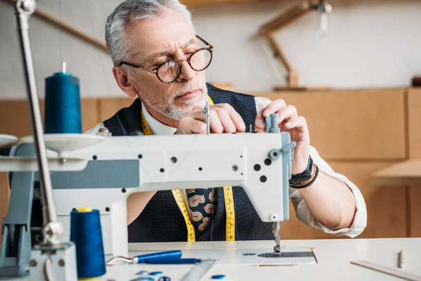 sastre maduro concentrado que trabaja con la máquina de coser moderna en taller
 - Foto, Imagen