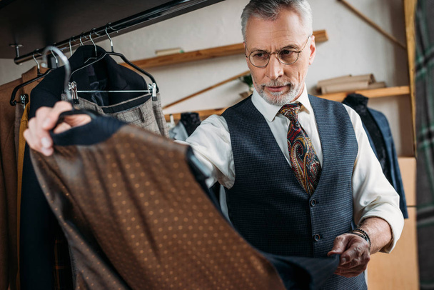 handsome mature tailor examining clothes at sewing workshop - Photo, Image